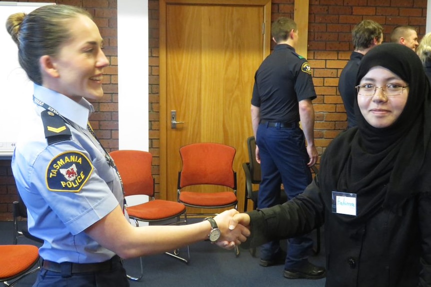 A female police officer and a woman in a black hijab shake hands