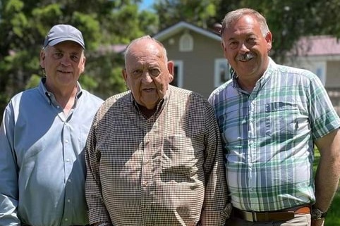 An old man flanked either side by two younger men.