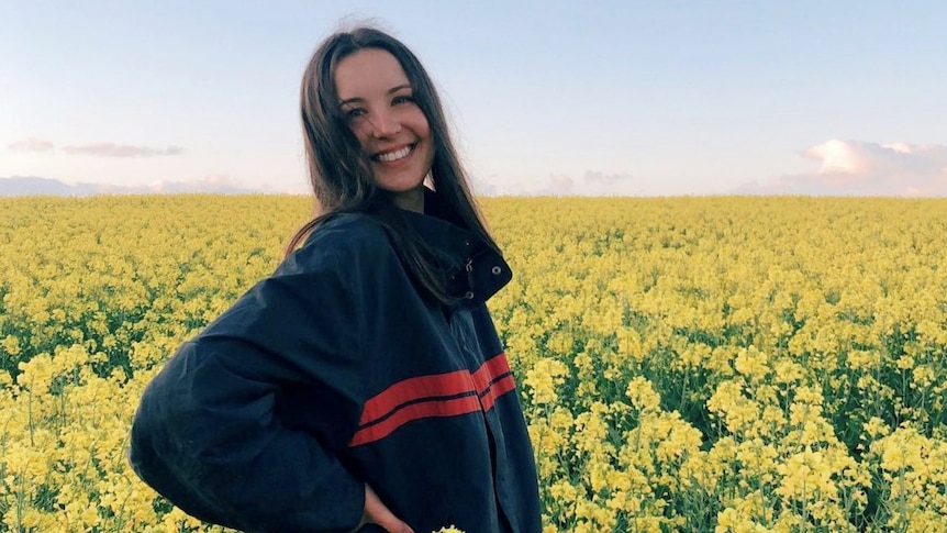 A young woman standing among yellow canola flowers