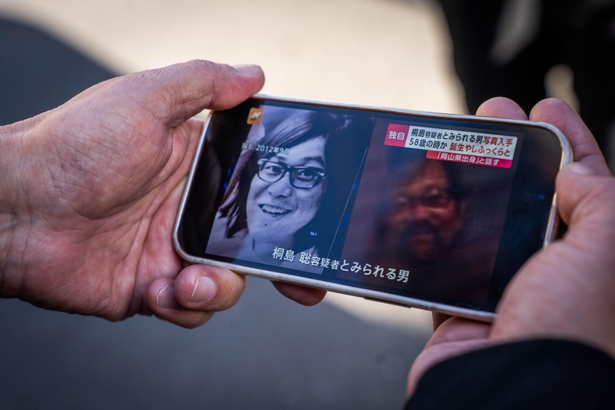A man holds a phone displaying a picture of a Japanese man
