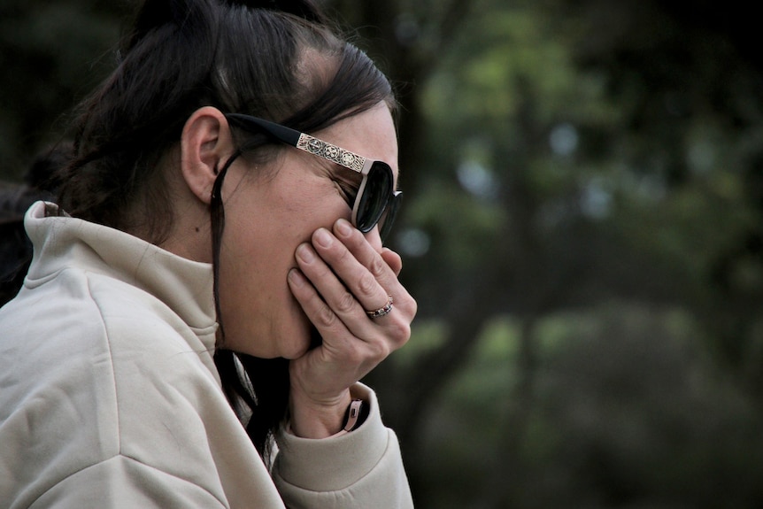 A woman wearing sunglasses with her hand over her mouth.