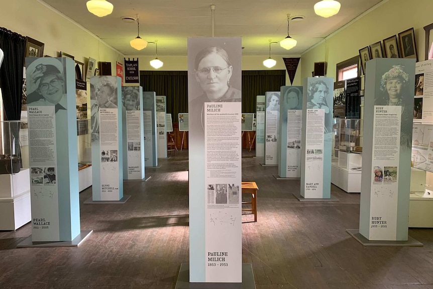 A light room is filled with 11 information signs. Each sign has a photo of a woman and writing underneath it.