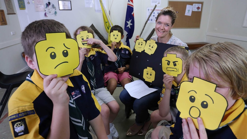 A woman reads to children who are holding up lego face masks