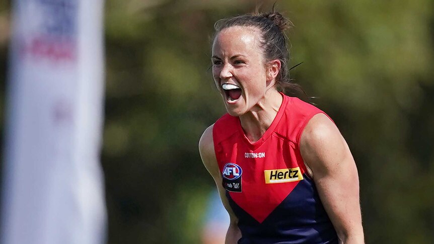 A Melbourne Demons AFLW player yells out as she celebrates her team winning a match.