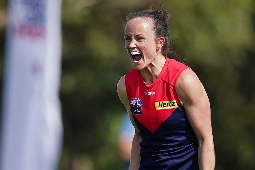 A Melbourne Demons AFLW player yells out as she celebrates her team winning a match.