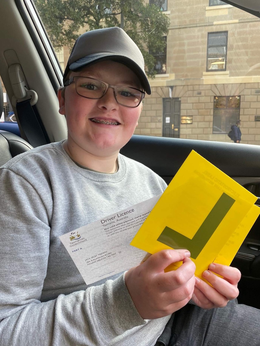 A boy wearing a cap holding a yellow 'L' plate.