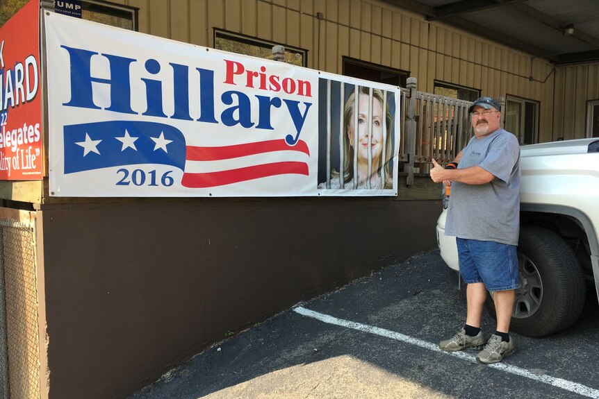 Logan County resident Tony Robison stands in front of a sign depicting Hillary Clinton behind bars.