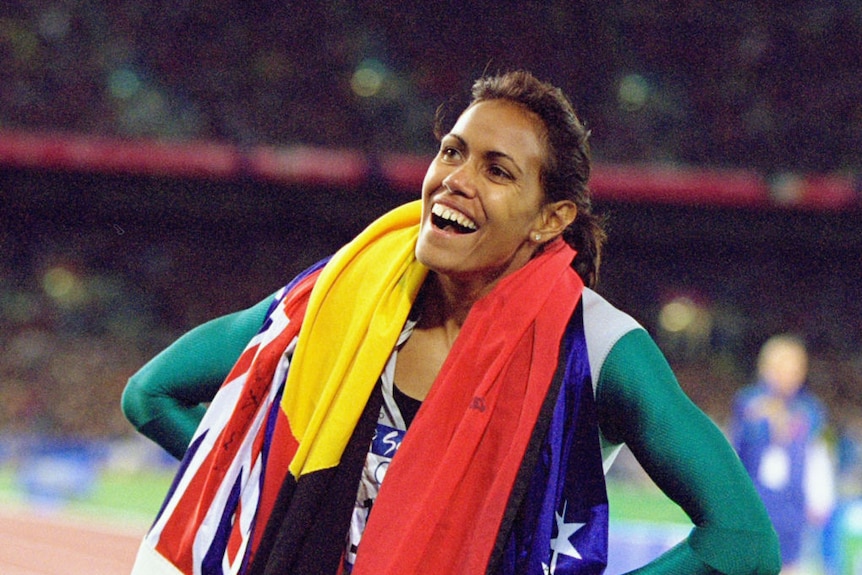 A woman smiles as the Australian and Aboriginal flag is draped over her body at the Olympic Games.