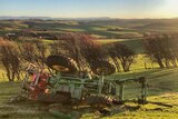 a tractor sits upturned on a hill in a paddock after rolling