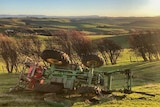 a tractor sits upturned on a hill in a paddock after rolling