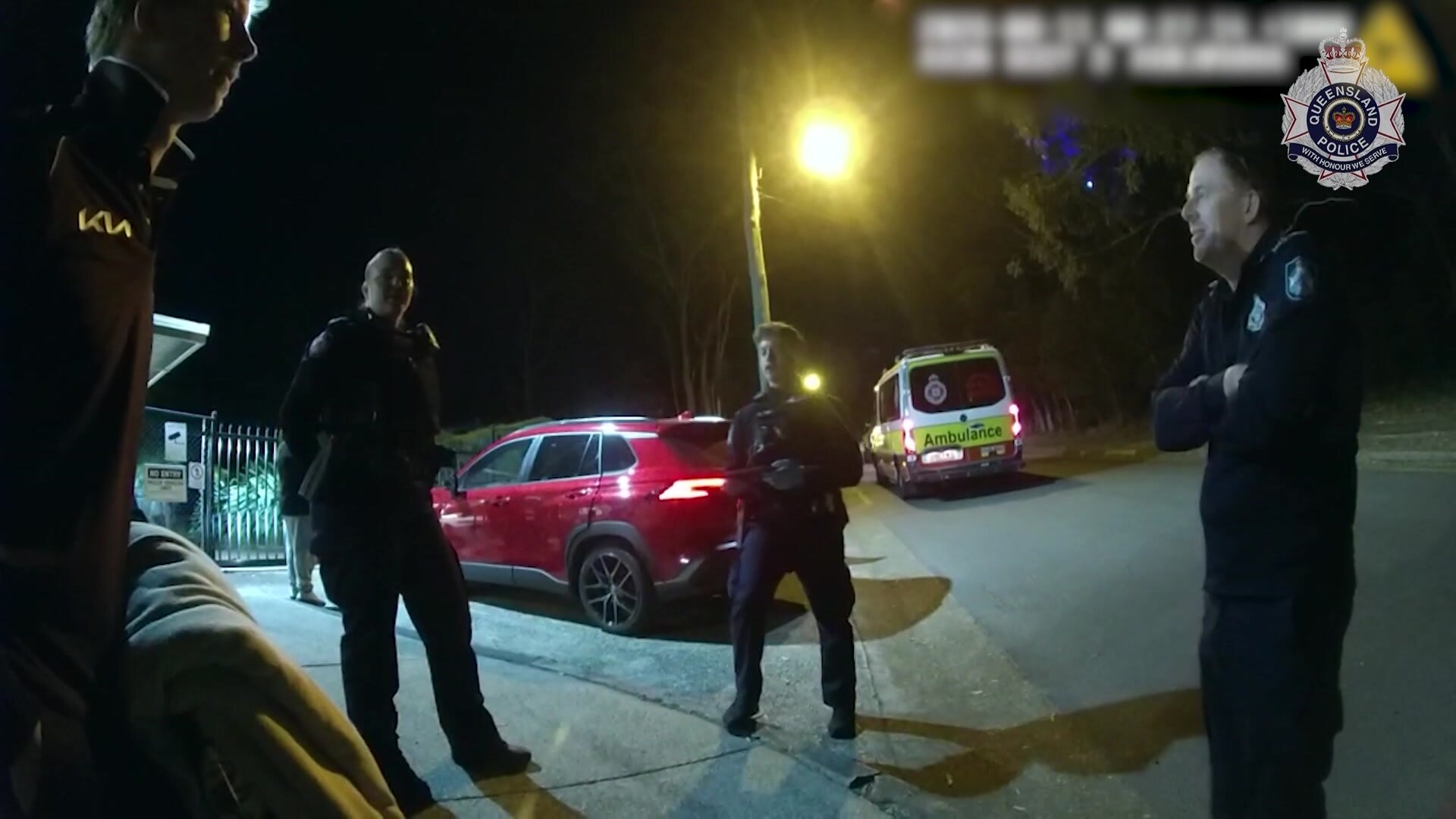Officers standing near a driveway with a red car parked in the background.