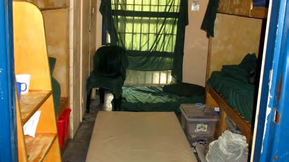 A crowded and messy prison cell with four bunk beds and mattresses on the floor.
