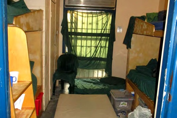 A crowded and messy prison cell with four bunk beds and mattresses on the floor.