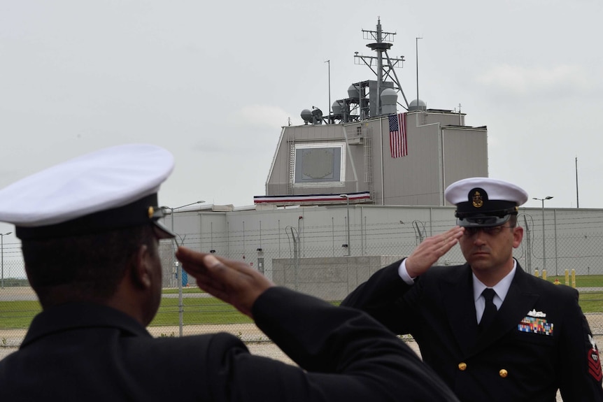 US Army servicemen salute during an inauguration ceremony with the defence system in the background.