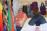 A woman standing next to a bed in a colourful bedroom with lots of coloured clothes hanging from the wall.