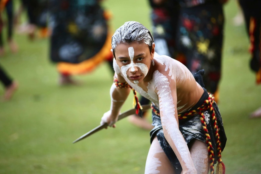 A bare chested Indigenous boy wearing face paint performs in a corroboree.