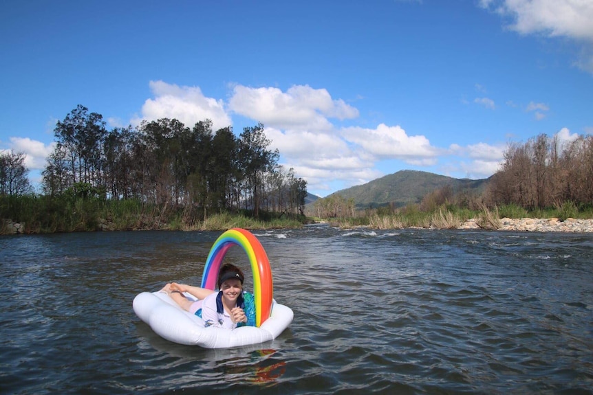 A young woman floats on a flotation device shaped like a cloud and rainbow in Cattle Creek