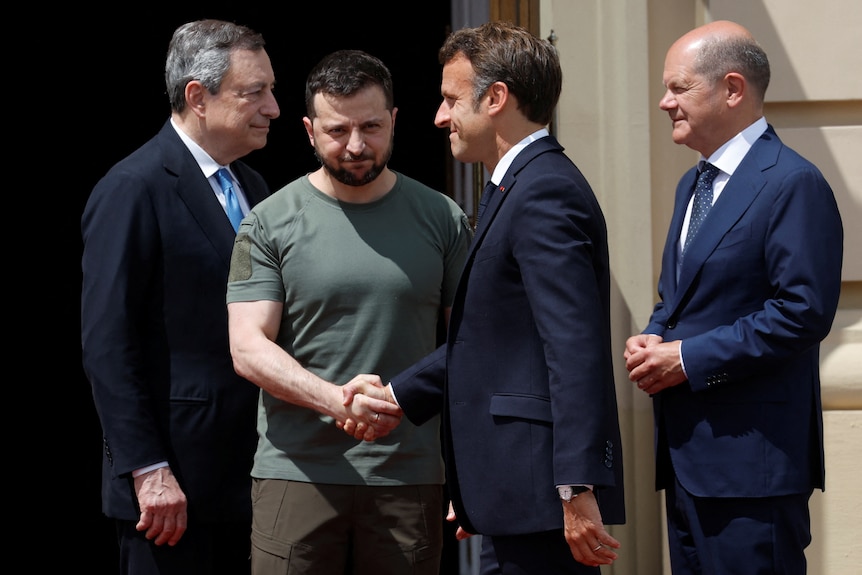 Four men stand beside each other as two of them shake hands.