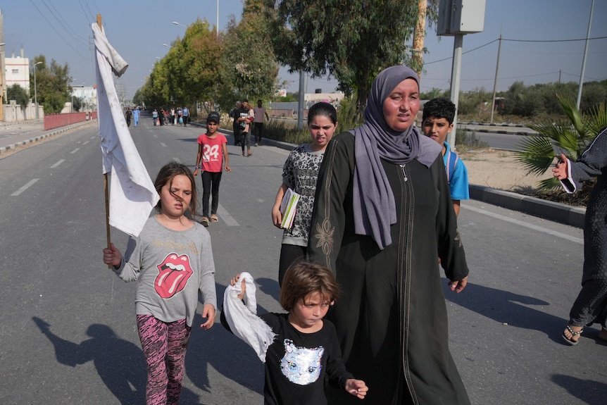 Young girl holds white flag made out of shirt while a younger child holds a white scrap next to an exhausted looking woman 
