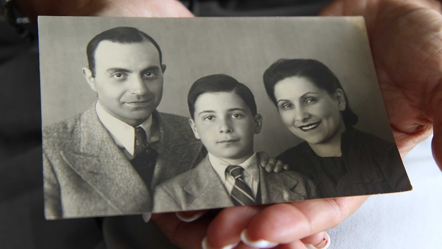 A photograph in a woman's hands shows and old black and white image of a father, mother and son.