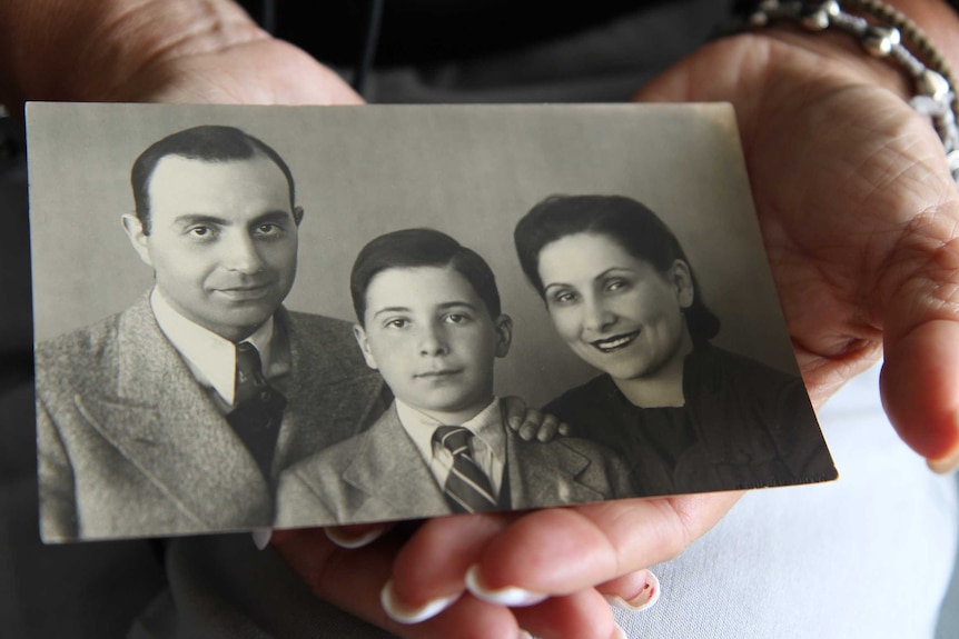 A photograph in a woman's hands shows and old black and white image of a father, mother and son.