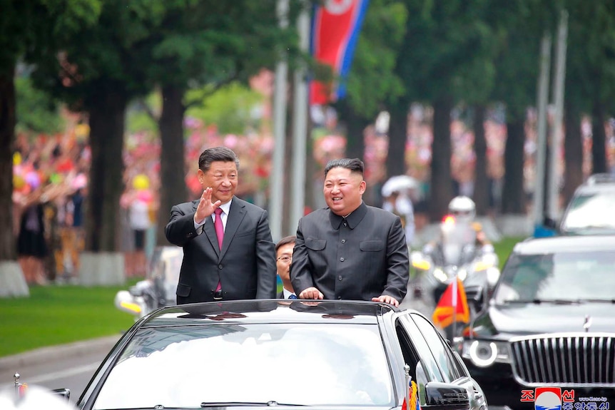 Two men standing in a driving limo waving to the crowd