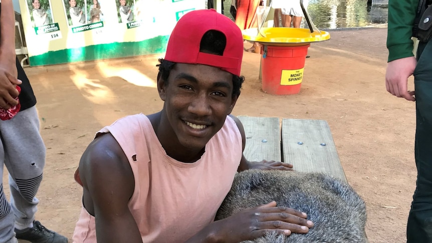 A smiling teenager wearing a backwards cap and a pink singlet petting wildlife. 