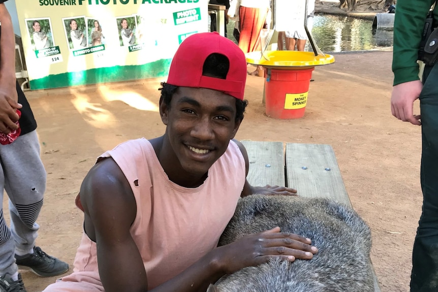 A smiling teenager wearing a backwards cap and a pink singlet petting wildlife. 
