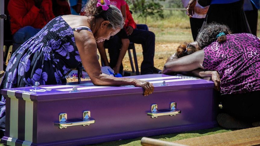 Indigenous women leaning on a purple coffin.