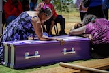 Indigenous women leaning on a purple coffin.