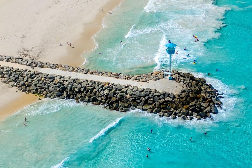 An aerial view of Perth City Beach in summer showing swimmers near a groyne of rock.