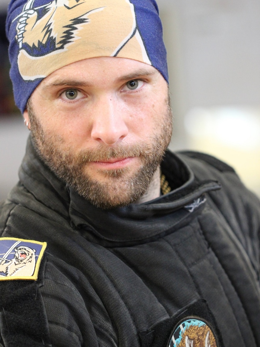 A bearded man wearing a bandana stares solemnly into the camera