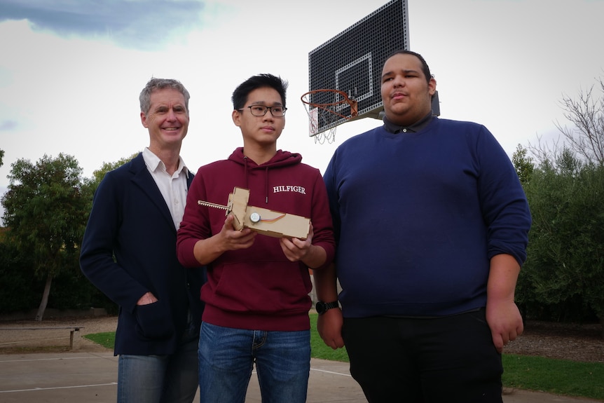 One middle aged man and two young men in front of a basketball hoop.