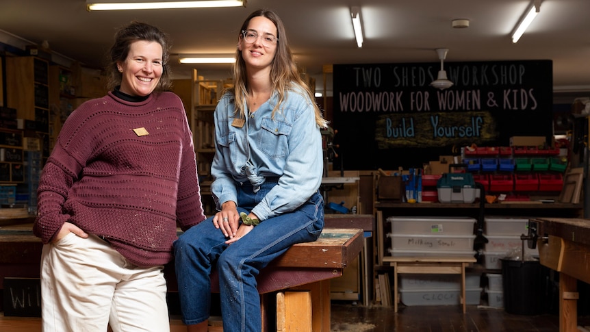Two women sitting on a wooden workshop bench