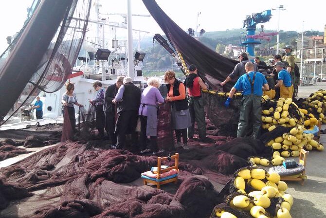 Women and boat crew mending a fishing net on Spanish wharf.