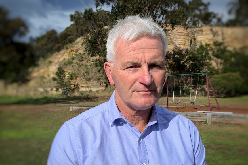 a grey-haired man in a blue business shirt with a hill background