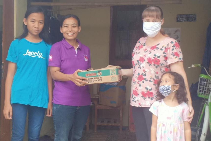 A woman and her daughter who are wearing a mask, handing food to another woman who is not wearing a mask.