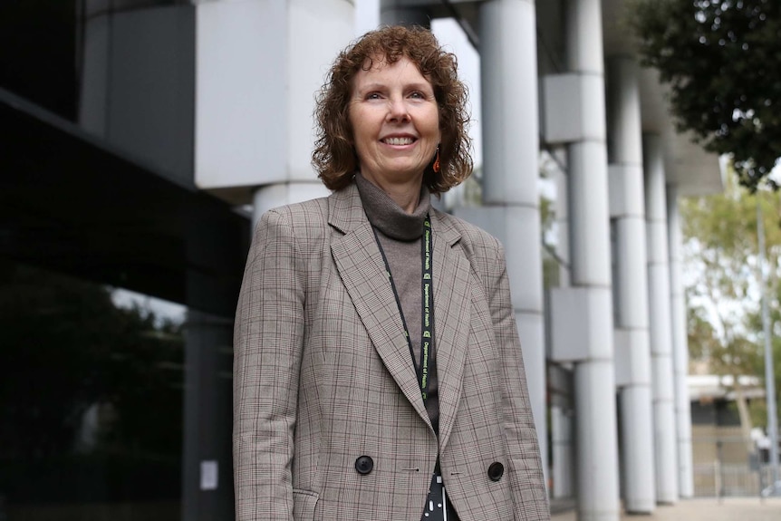 A mid-shot of Robyn Lawrence standing in an office with her arms folded looking serious.