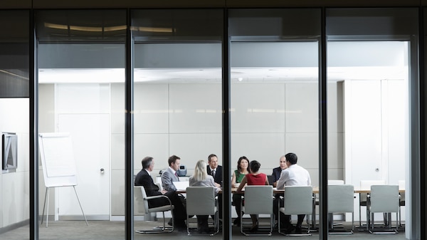 An image taken from the exterior of a group of staff sitting around a board table .