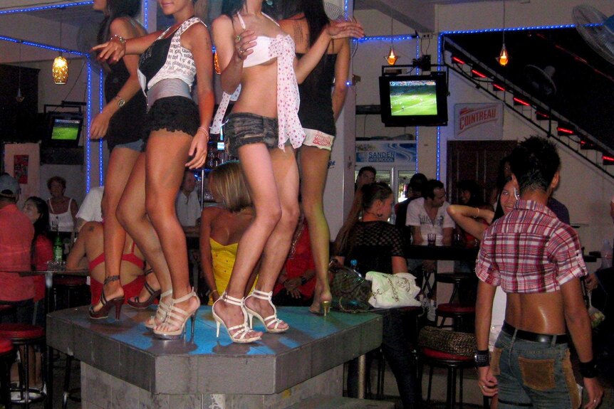 Thai dancers in short skirts and shorts dance on a bar in a nioghtclub