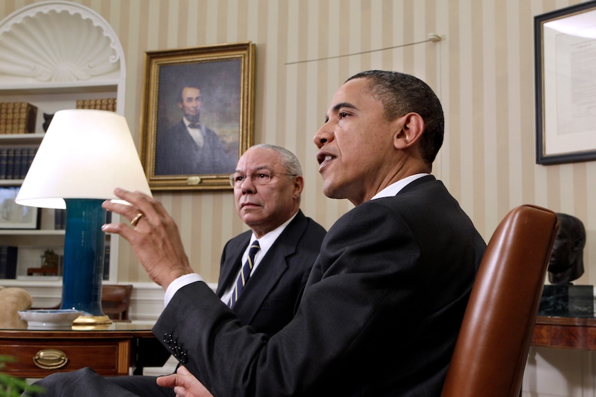 Barack Obama speaks, while Colin Powell sits beside him in the Oval Office in the White House.