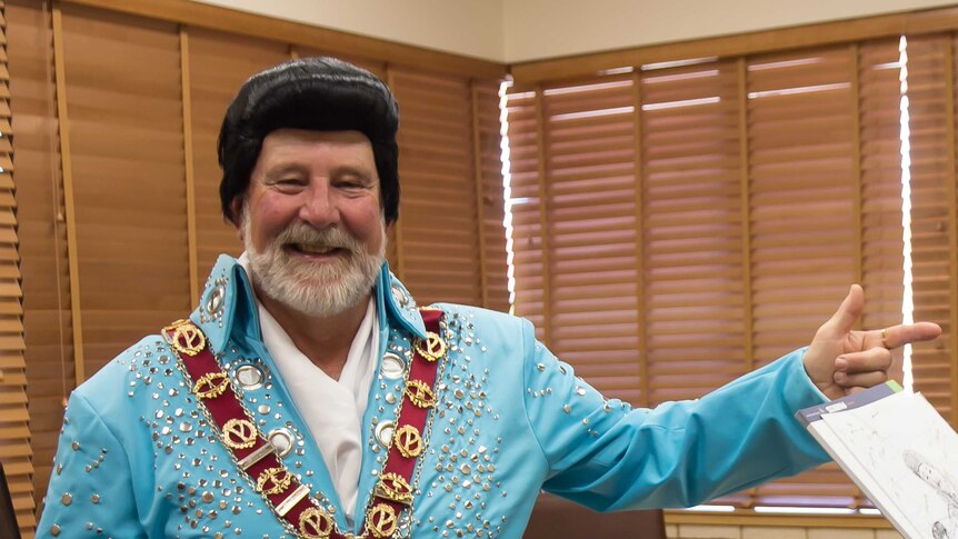 A man in an Elvis wig and blue studded jumpsuit wearing a mayor's chain