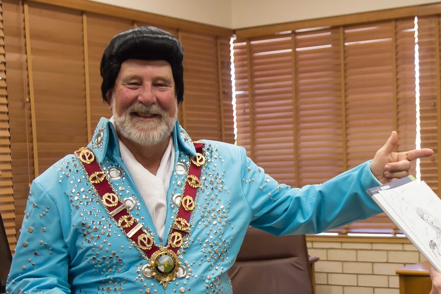 A man in an Elvis wig and blue studded jumpsuit wearing a mayor's chain