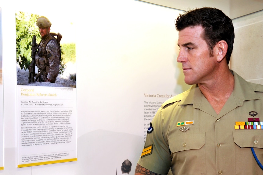 a man wearing his defence uniform looking at a picture of himself in combat gear in a war zone