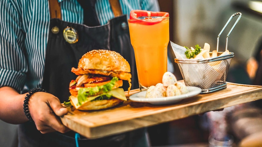 An unidentified fast food worker carries a tray containing a drink, hamburger and chips