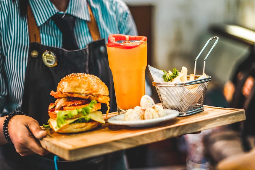 A waiter's hands hold a tray with a burger and drink on it.
