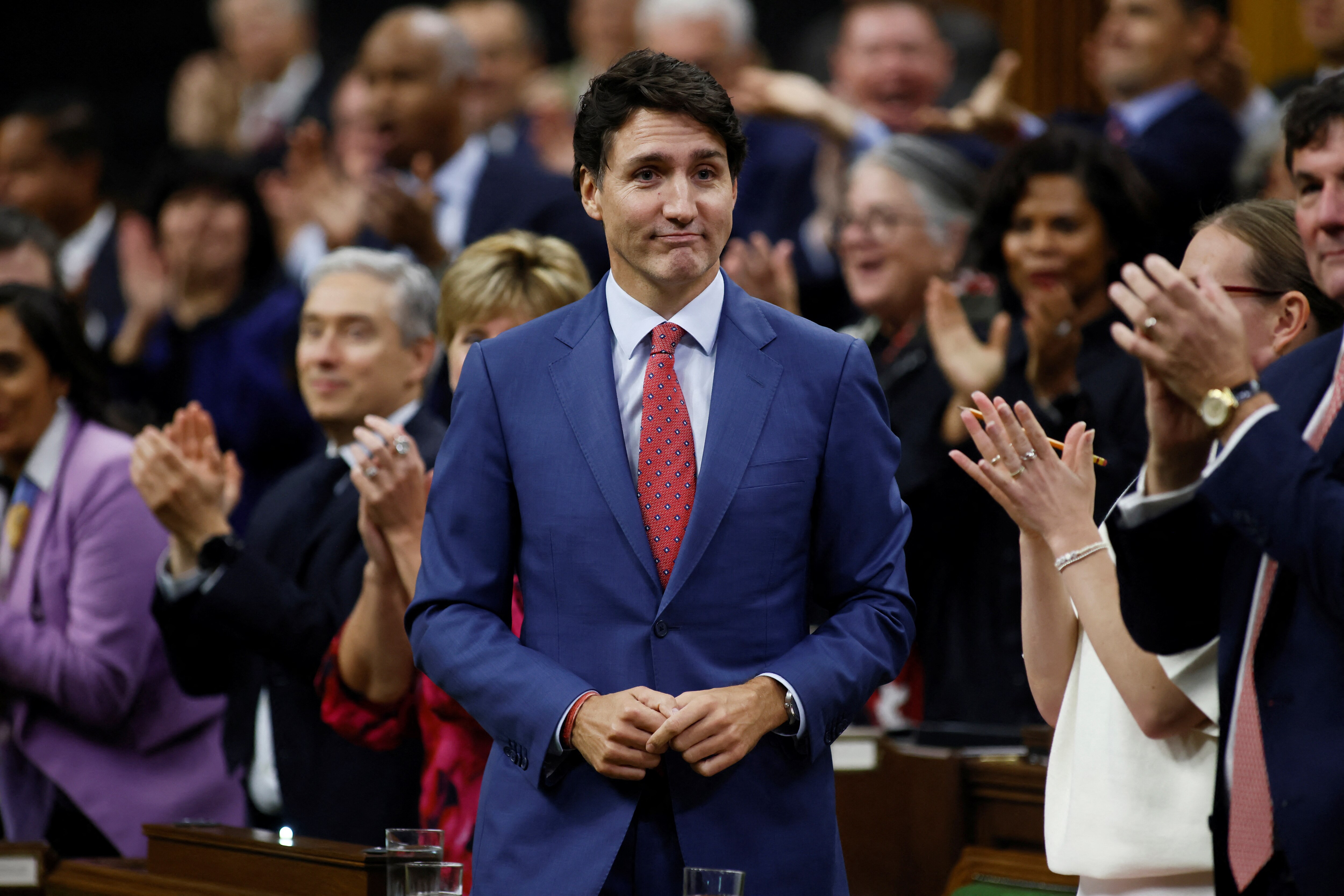 a man in a navy blue suit and red tie is applauded in canada's house of commons