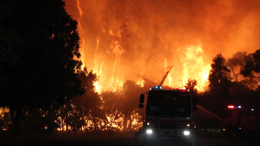 Flames and smoke light up the sky behind a fire truck.