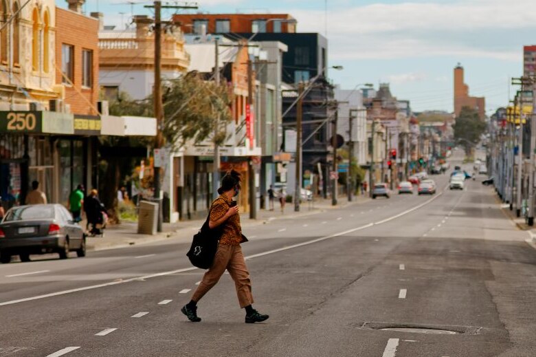 A person wearing an orange shirt and tan pants walks across an inner-city street. Very few people or cars around