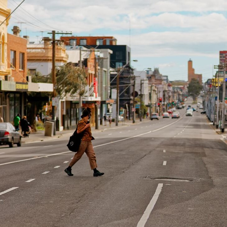A person wearing an orange shirt and tan pants walks across an inner-city street. Very few people or cars around